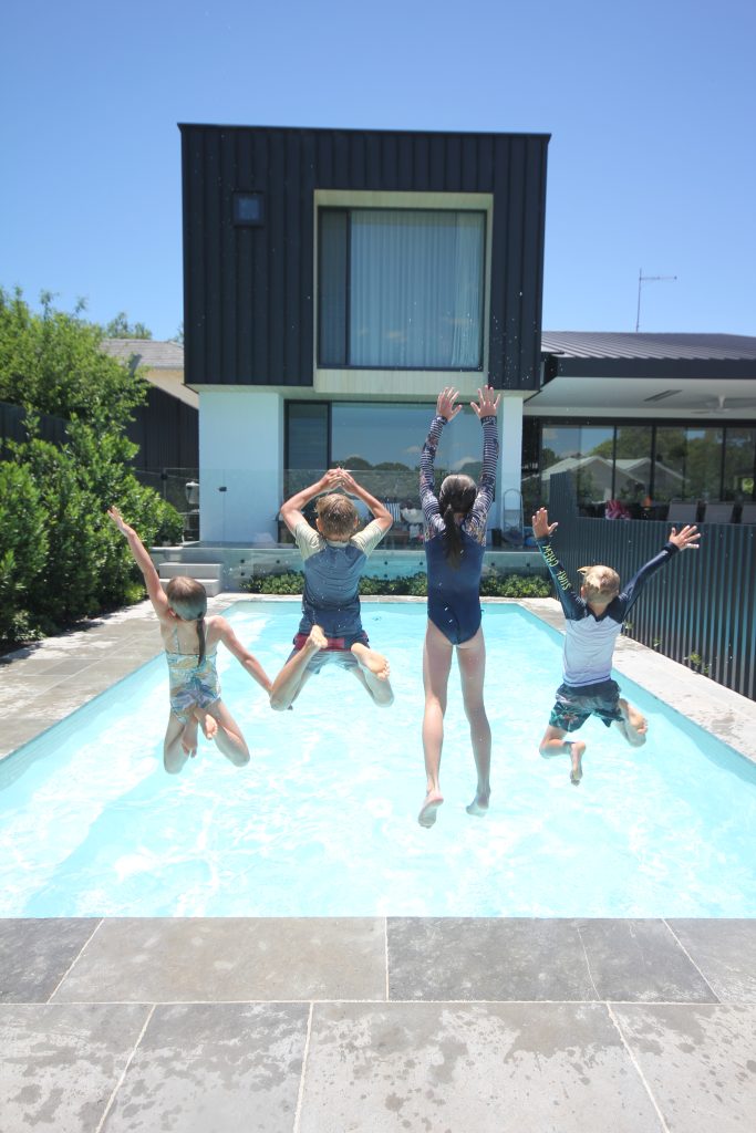 Four children jumping into a pool with blue skies