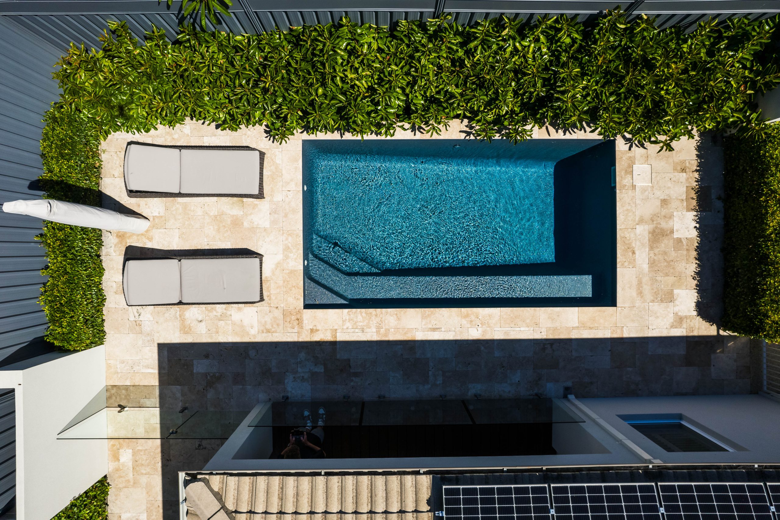Aerial view of Aqua Technics Sovereign fibreglass pool in Moonlight with integrated spa, travertine paving, lush hedging, and sun loungers in a compact backyard